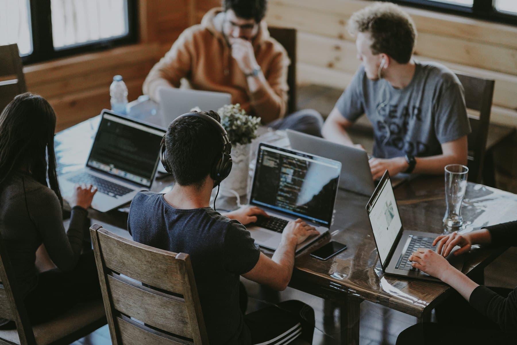 Four people working side by side on laptops at a shared table.